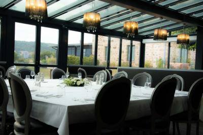 Salle de restaurant moderne avec une grande table en bois, suspensions noires et étagères de bouteilles illuminées.