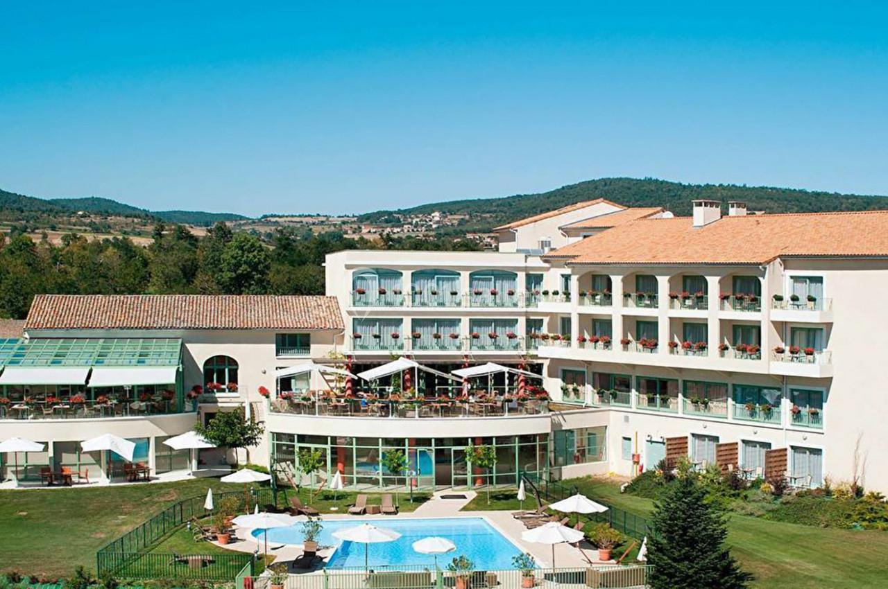 Hôtel avec piscine extérieure, terrasses et jardin, entouré de collines sous un ciel bleu clair.