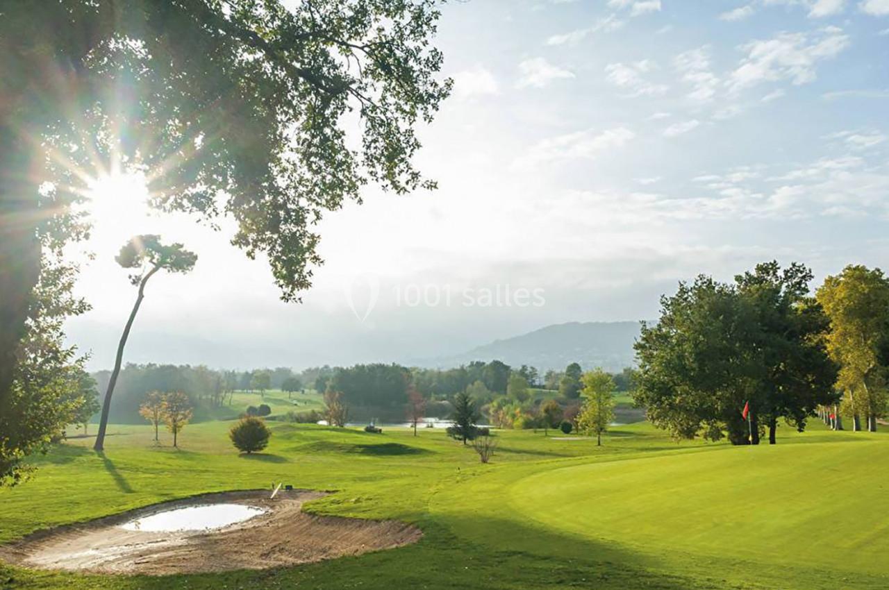 Paysage de golf avec un terrain verdoyant, des arbres, un bunker de sable et un soleil éclatant à l'horizon.