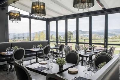 Salle de restaurant moderne avec une grande table en bois, suspensions noires et étagères de bouteilles illuminées.