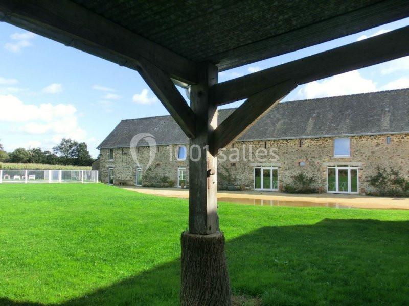 Vue d'une grande bâtisse en pierre avec toit en ardoise, entourée de pelouses, prise depuis un abri en bois.