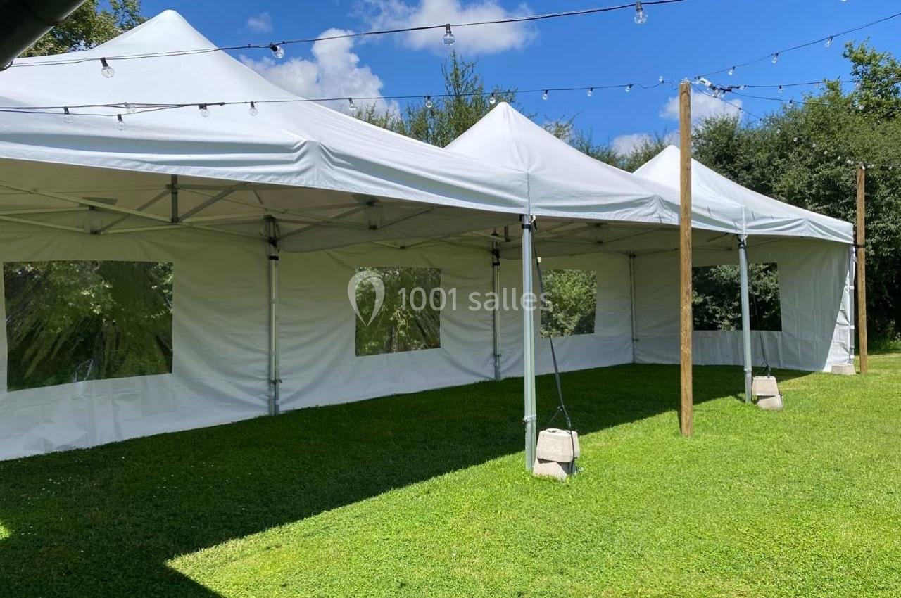 Tentes blanches installées sur une pelouse, entourées d'arbres, avec des guirlandes lumineuses suspendues.
