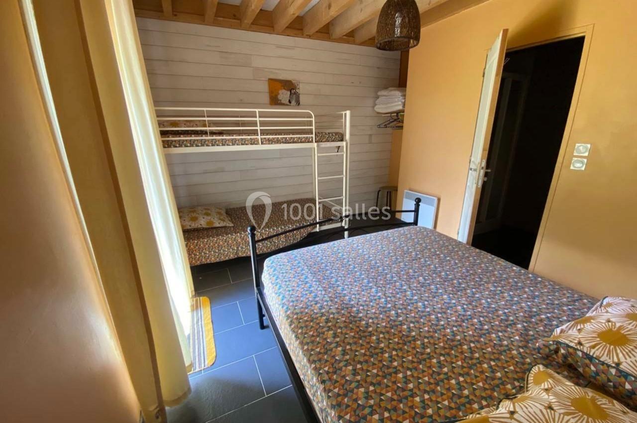 Chambre avec un lit double, des lits superposés, murs en bois clair et plafond avec poutres apparentes.