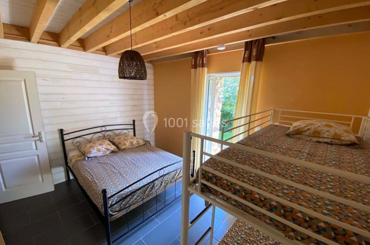 Chambre avec un lit double, des lits superposés, murs en bois clair, plafond avec poutres apparentes et fenêtre donnant sur…