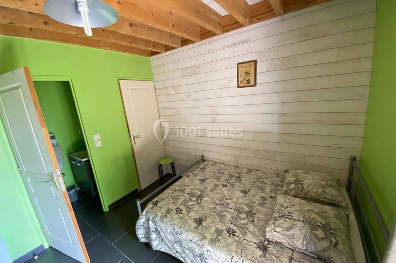 Chambre avec lit double, murs verts et en bois clair, plafond avec poutres apparentes, porte ouverte sur une salle d'eau.