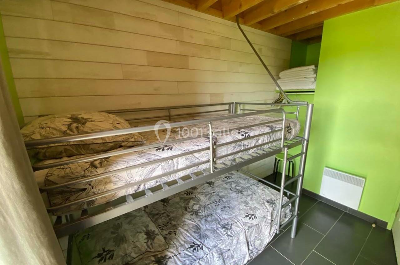 Lit superposé en métal dans une chambre aux murs verts et bois, avec des draps à motifs floraux et des serviettes pliées.