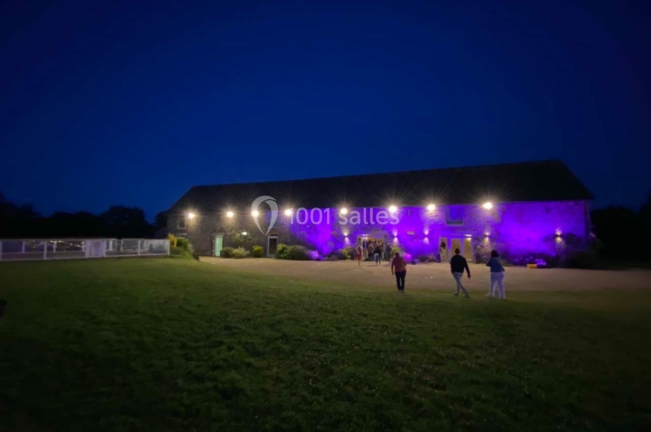 Bâtiment en pierre éclairé par des lumières violettes et blanches, avec quelques personnes marchant sur une pelouse au…