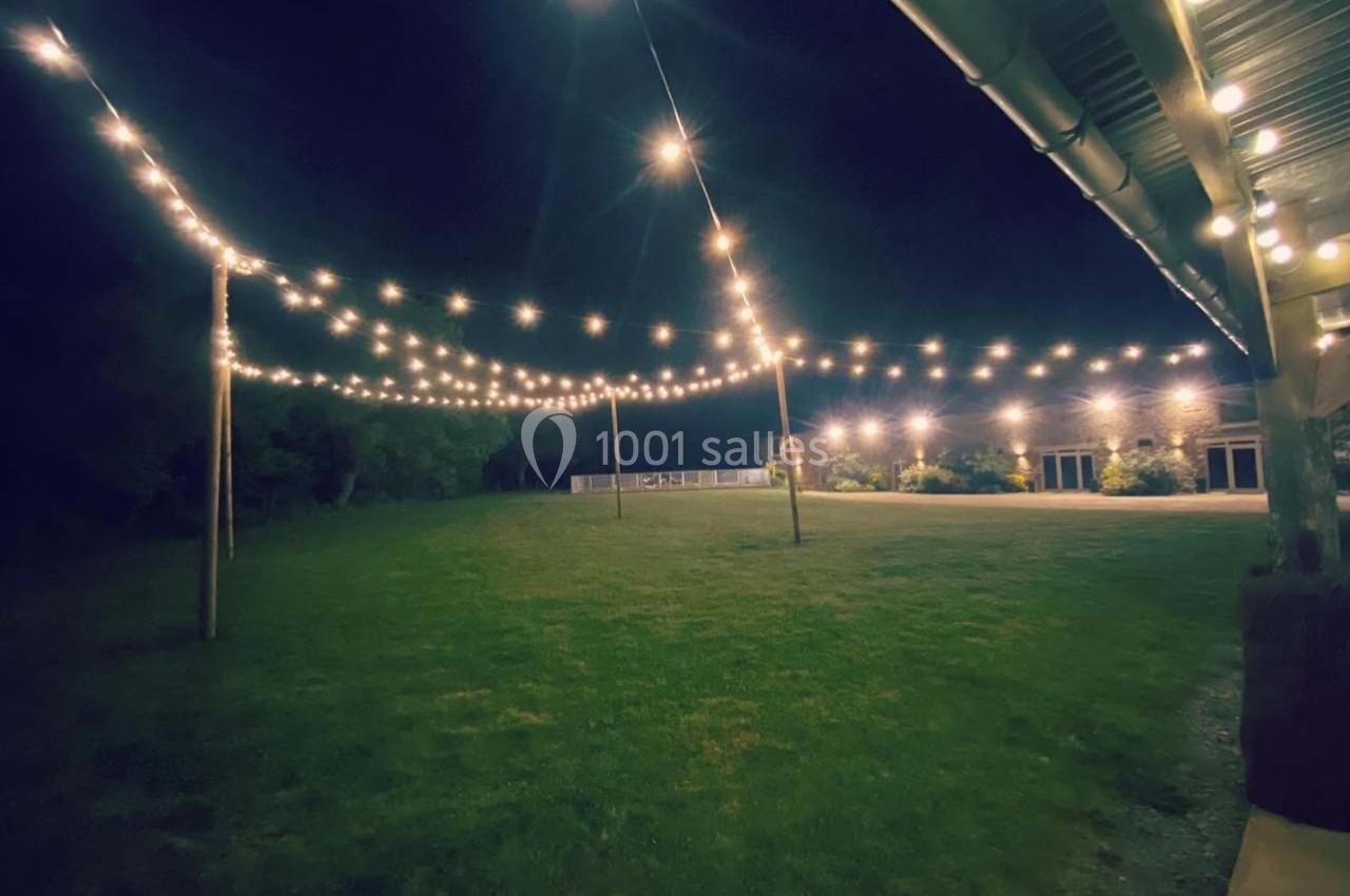 Guirlandes lumineuses suspendues au-dessus d'une pelouse la nuit, éclairant un espace extérieur près d'un bâtiment.