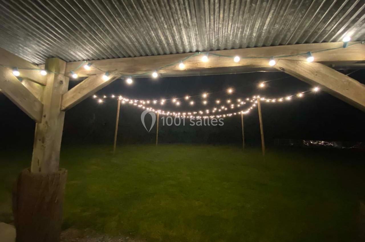 Guirlandes lumineuses suspendues sous un toit en bois, éclairant une pelouse dans l'obscurité.