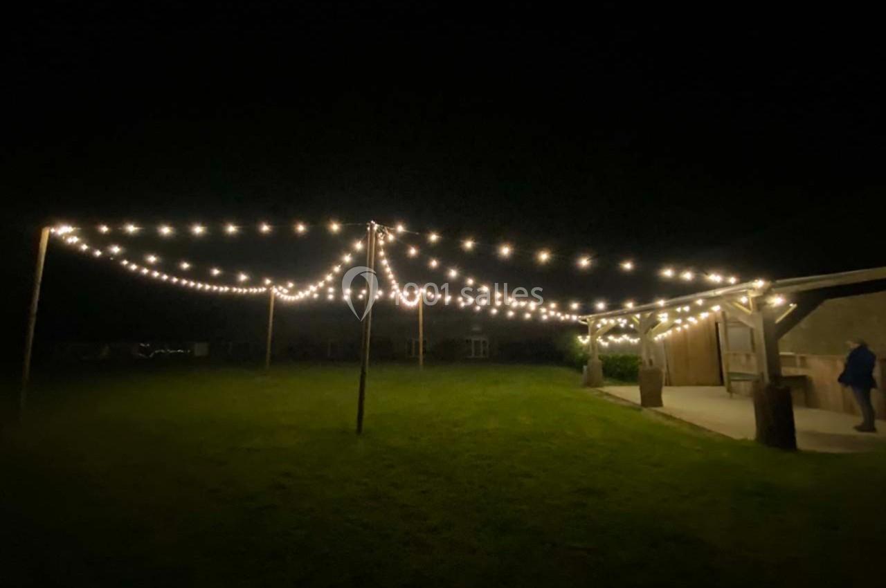 Guirlandes lumineuses suspendues en extérieur, éclairant un espace herbeux sombre près d'une structure en bois.