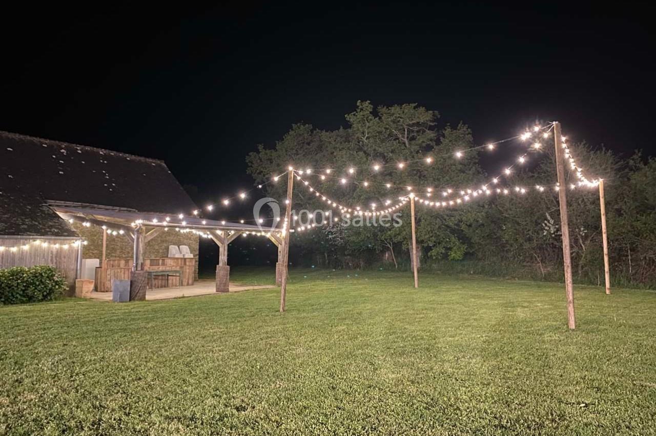 Guirlandes lumineuses suspendues au-dessus d'une pelouse, près d'une structure en bois, dans un cadre nocturne.