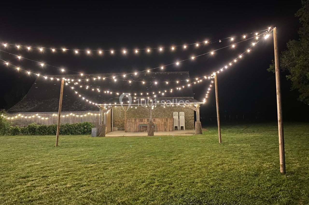 Guirlandes lumineuses suspendues au-dessus d'une pelouse, éclairant une petite structure en bois dans l'obscurité.