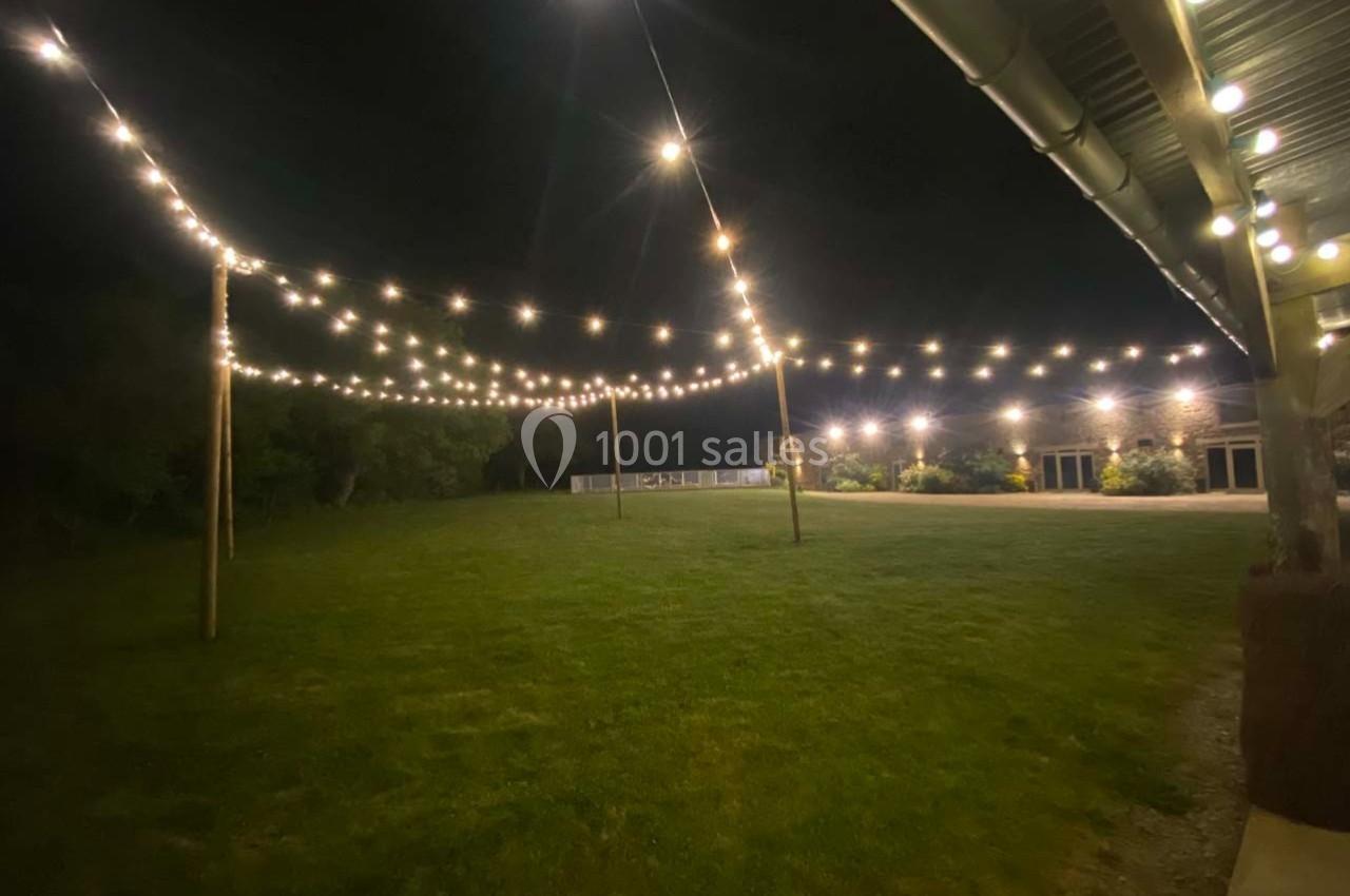 Guirlandes lumineuses suspendues au-dessus d'une pelouse éclairée, près d'un bâtiment en soirée.