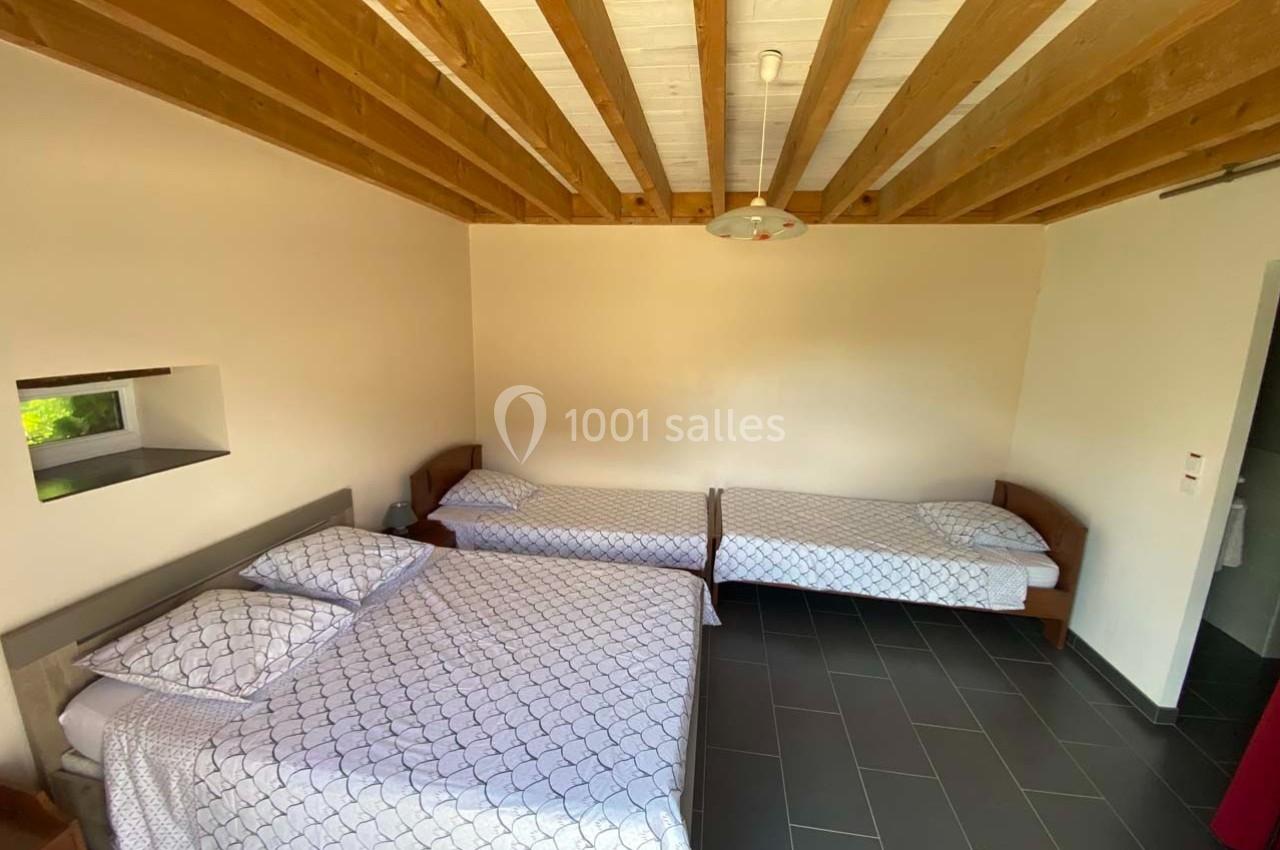 Chambre avec un lit double et deux lits simples, parquet sombre, plafond en bois et lumière naturelle.