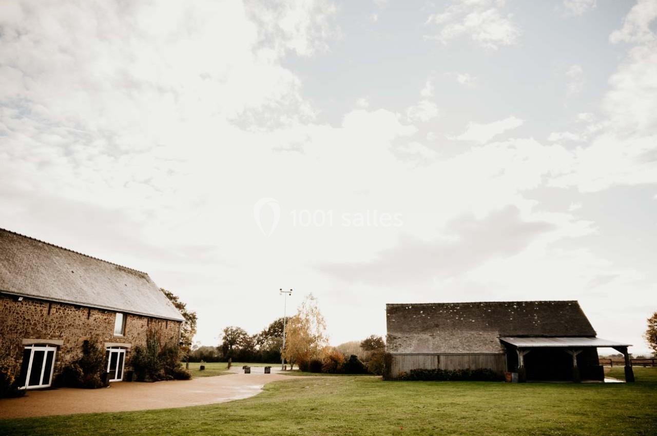 Deux bâtiments en pierre avec toits en ardoise entourés d'une pelouse et d'arbres sous un ciel partiellement nuageux.