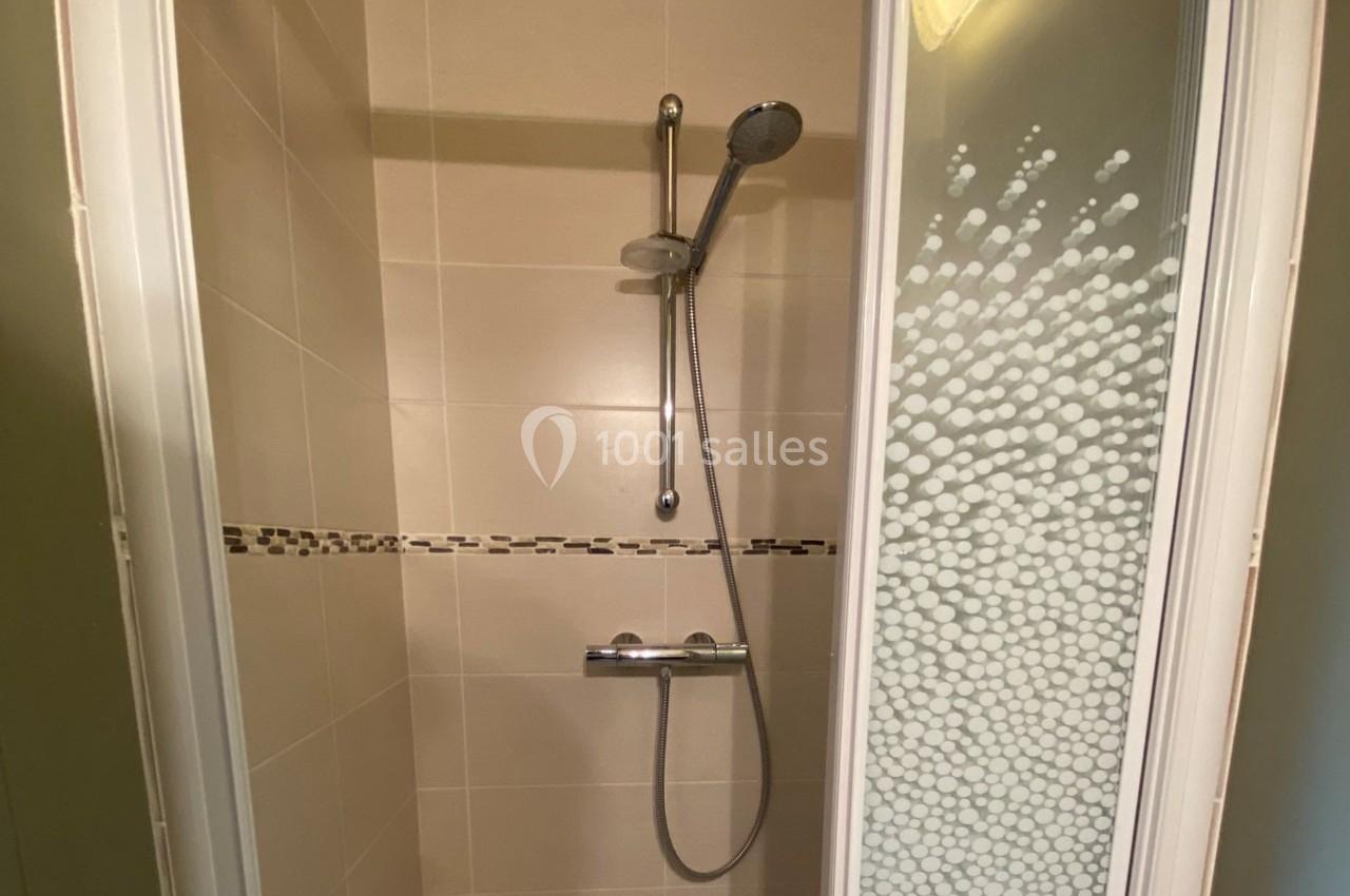 Douche avec carrelage beige, paroi vitrée décorée de motifs, équipée d'une pomme de douche et d'un mitigeur.