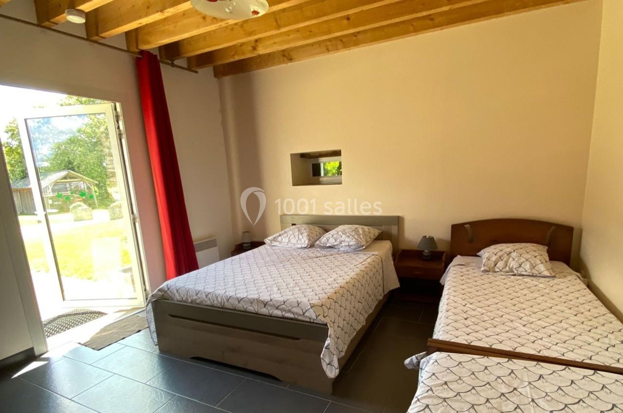 Chambre lumineuse avec un lit double, un lit simple, des poutres apparentes et une porte ouverte sur un jardin.