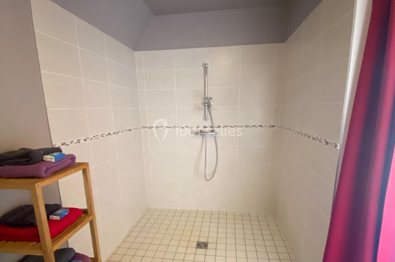 Douche à l'italienne avec carrelage clair, équipée d'une barre de douche, à côté d'une étagère en bois.