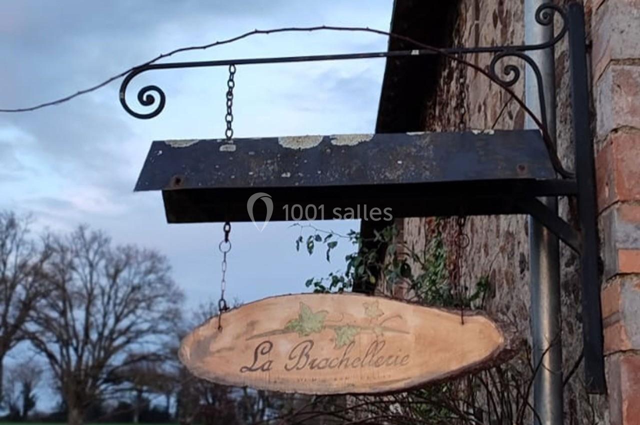 Enseigne en bois suspendue à une structure métallique, portant l'inscription ’La Brachellerie’, devant un mur en briques.