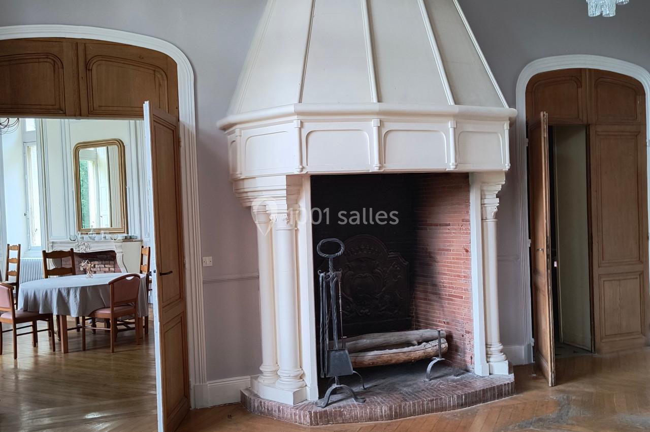 Cheminée ancienne en pierre blanche dans une pièce avec parquet en bois, portes ouvertes donnant sur une salle à manger.
