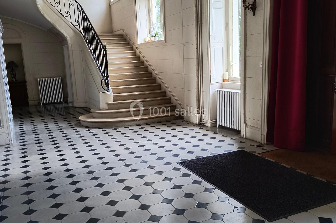 Hall d'entrée lumineux avec sol en carreaux noirs et blancs, escalier en colimaçon et grandes fenêtres.