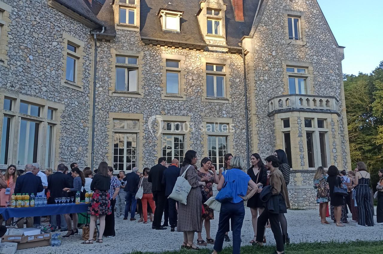 Groupe de personnes rassemblées devant un château en pierre lors d'un événement en plein air par temps ensoleillé.