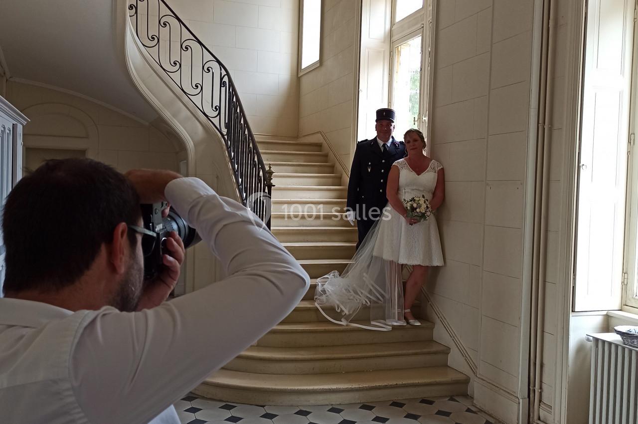 Un photographe capture un couple de mariés posant près d'un escalier dans un intérieur lumineux.