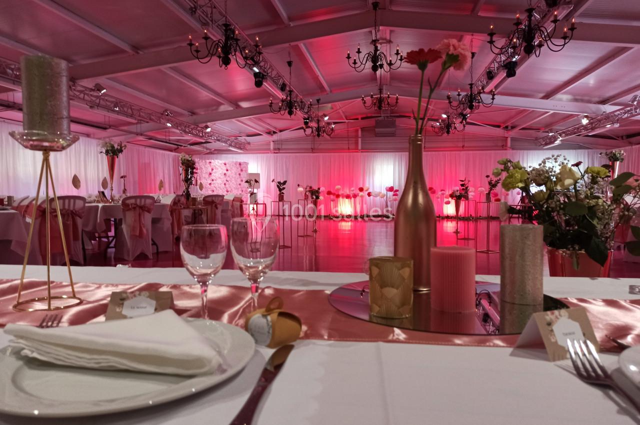 Salle de réception décorée avec des tables dressées, des chandeliers suspendus et une ambiance lumineuse rose.