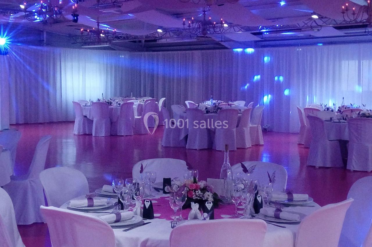 Salle de réception décorée avec des tables rondes dressées, nappes blanches et éclairage tamisé bleu.