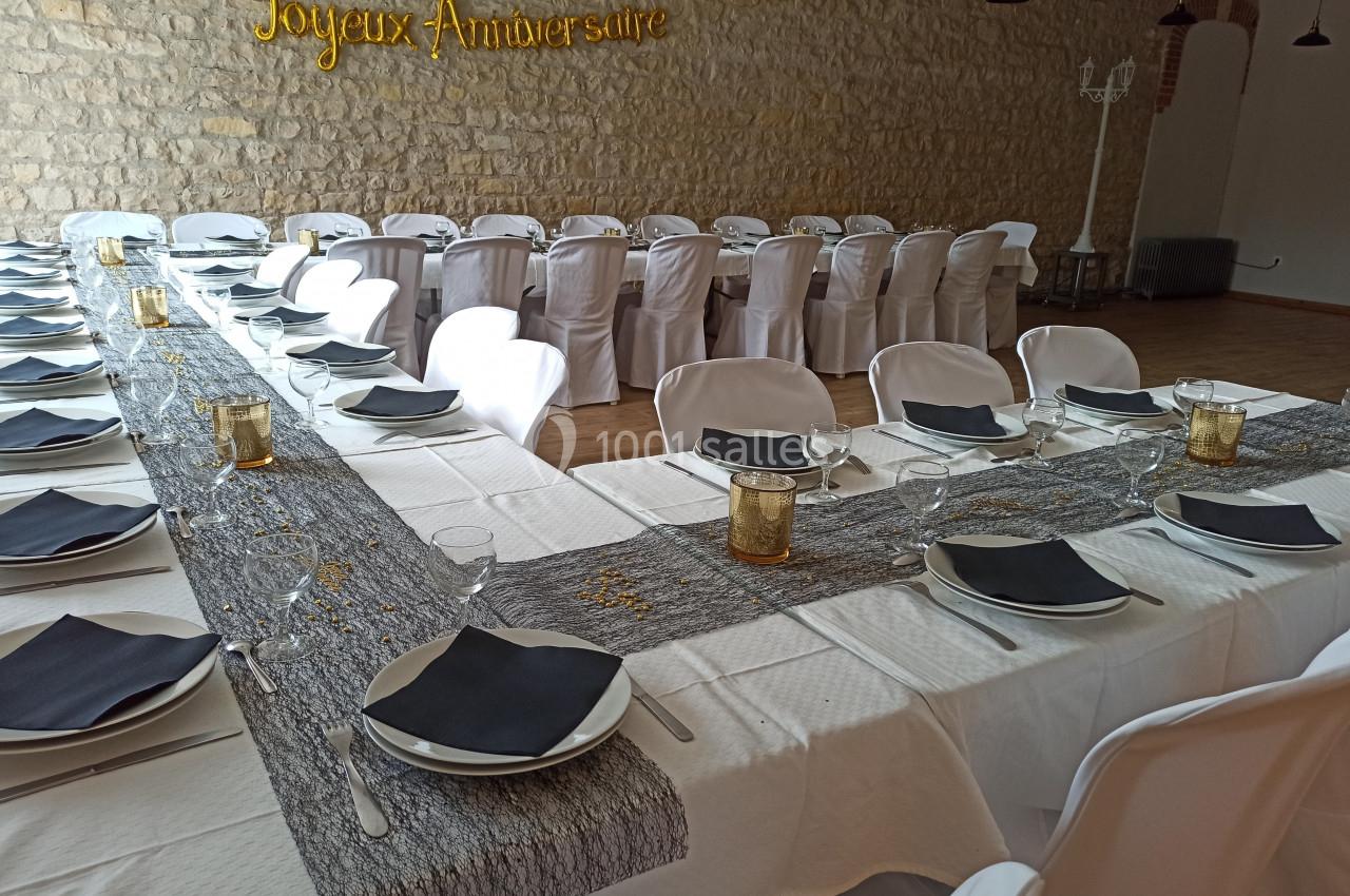 Salle décorée pour un anniversaire avec tables dressées, nappes blanches, serviettes noires et bougies dorées.