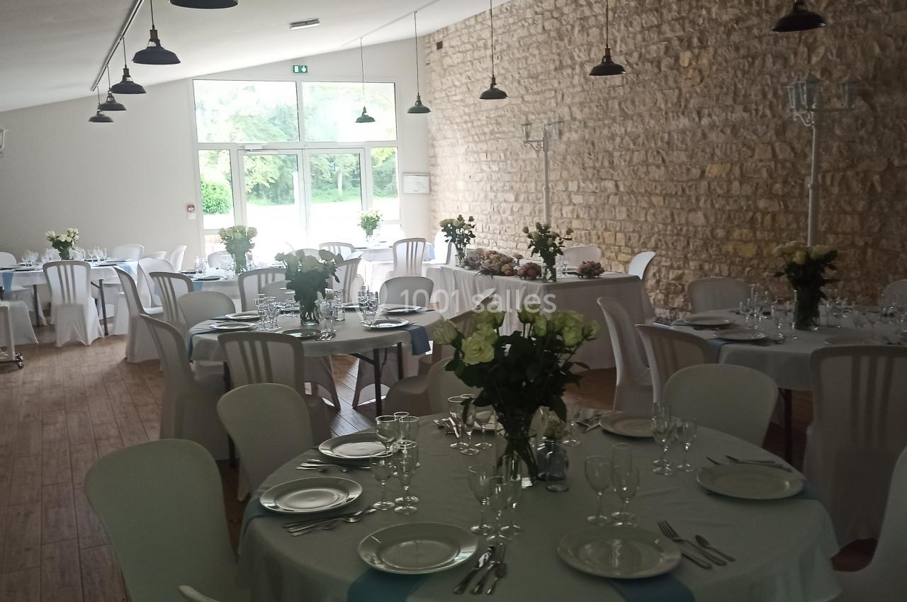 Salle de réception lumineuse avec tables rondes dressées, nappes blanches, chaises assorties et décoration florale.