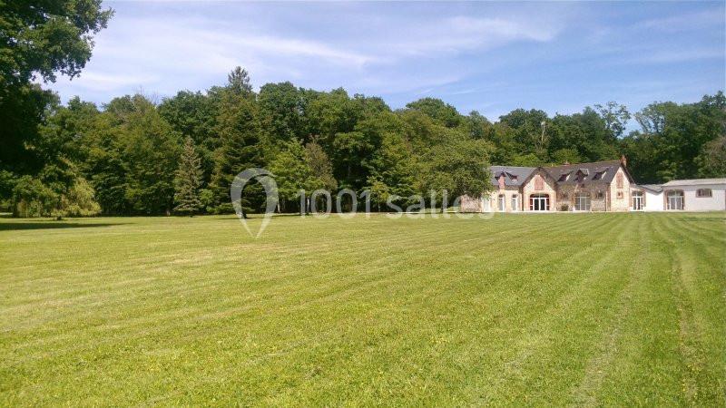 Grande pelouse verdoyante bordée d'arbres, avec une maison en pierre et toit en ardoise visible à droite.