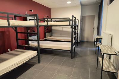 Dortoir avec lits superposés en métal noir, murs rouges et blancs, sol en carrelage foncé, éclairage au plafond.