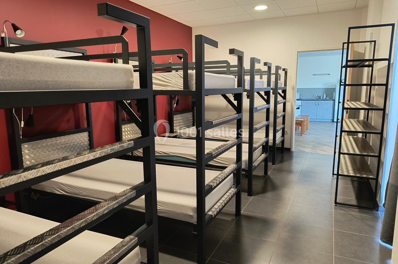 Dortoir avec lits superposés en métal noir, murs rouges et blancs, sol en carrelage foncé, éclairage au plafond.
