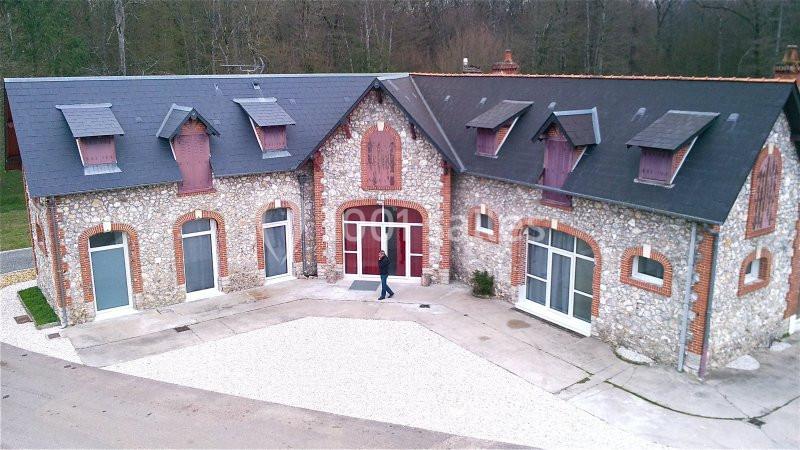 Bâtiment en pierre avec toit en ardoise, fenêtres mansardées et grande entrée vitrée, entouré de végétation.