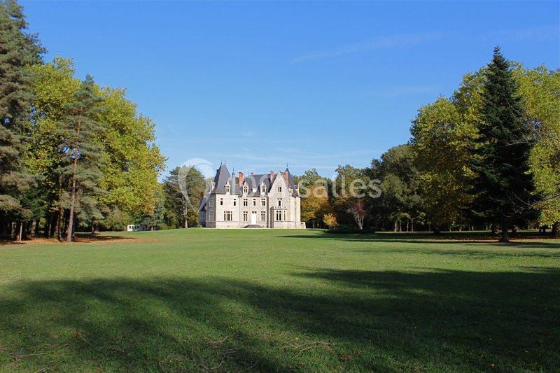 Château entouré d'un vaste parc verdoyant avec des arbres sous un ciel bleu clair.
