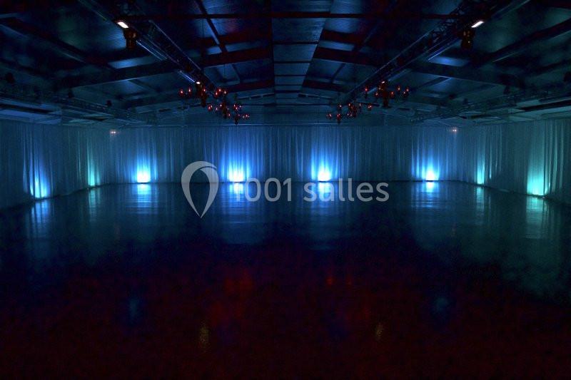 Salle vide avec éclairage tamisé bleu et rideaux blancs couvrant les murs, plafond avec structures métalliques.