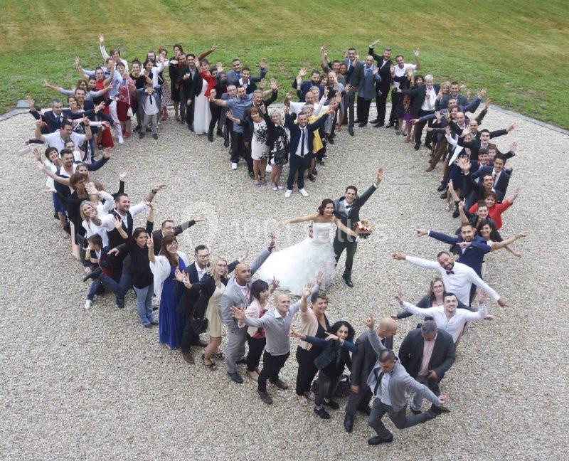 Groupe de personnes formant un cœur autour d'un couple de mariés sur une allée gravillonnée, avec pelouse en arrière-plan.