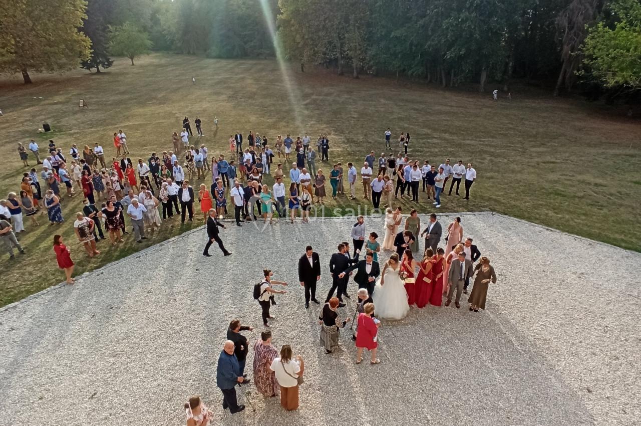 Groupe de personnes rassemblées en extérieur sur une esplanade, entourée de pelouse et d'arbres.