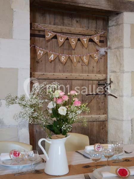 Décoration de mariage avec une porte en bois ornée d'une guirlande ’Juste Mariés’ et une table dressée avec fleurs.