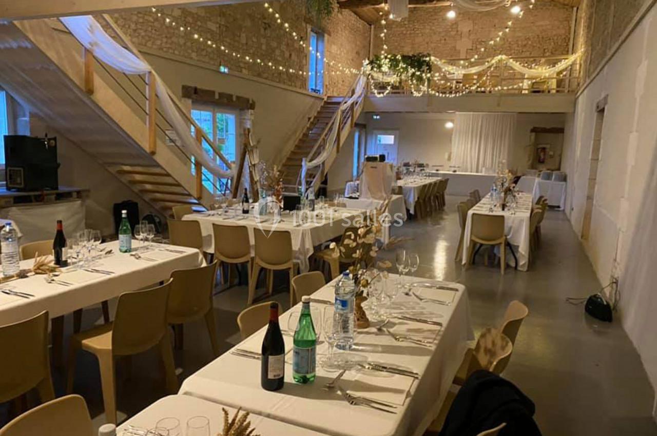 Salle de réception décorée avec des tables dressées, des guirlandes lumineuses et un plafond en bois apparent.