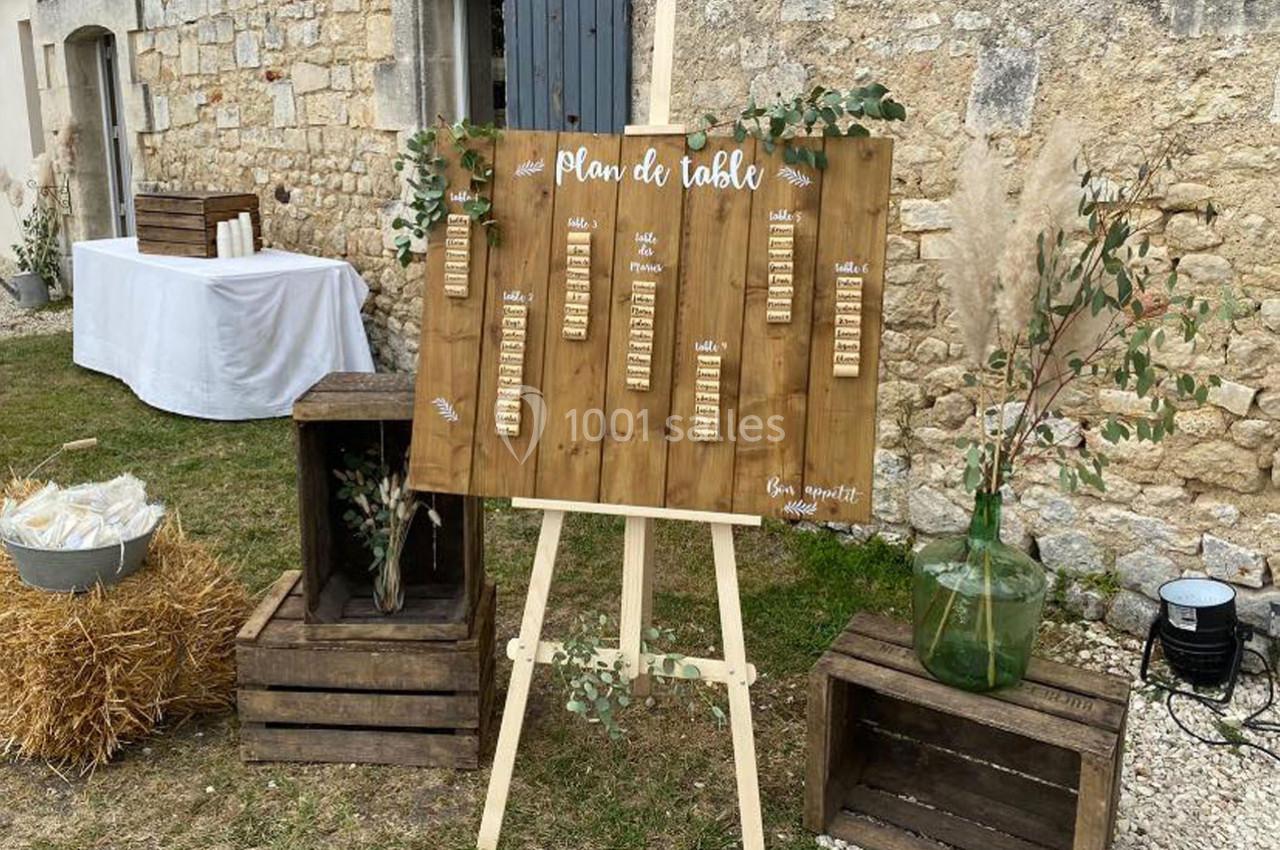Plan de table en bois sur un chevalet, entouré de caisses en bois, décorations végétales et bottes de paille.