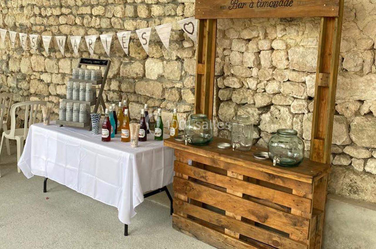 Stand de boissons avec un bar à limonade en bois et une table proposant des bouteilles et des bocaux, devant un mur en…