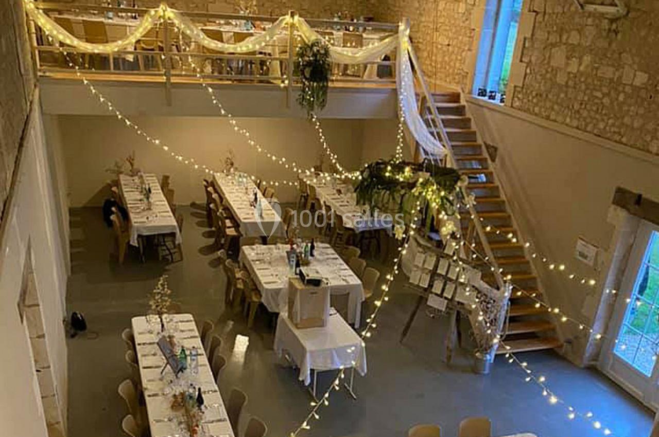 Salle de réception décorée avec des guirlandes lumineuses, des tables dressées et un escalier en bois.