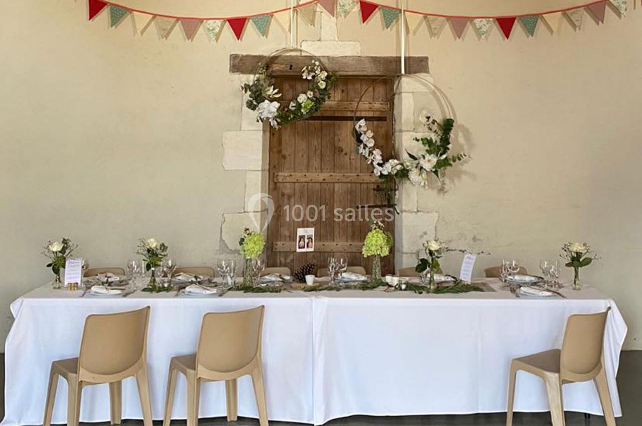 Table décorée pour un événement avec nappes blanches, fleurs, vaisselle élégante et guirlande suspendue en arrière-plan.
