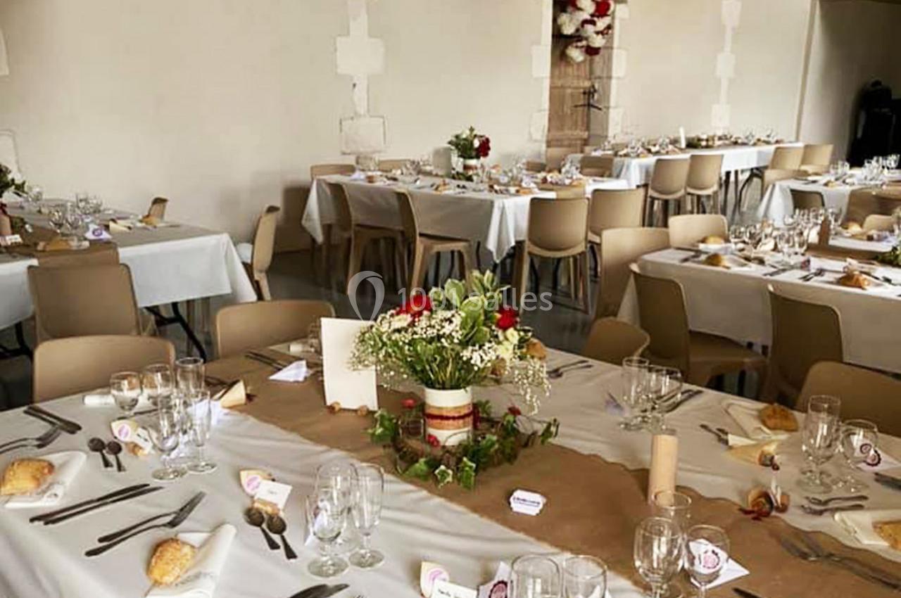 Salle de réception décorée avec des tables dressées, nappes blanches, centres de table fleuris et couverts disposés.
