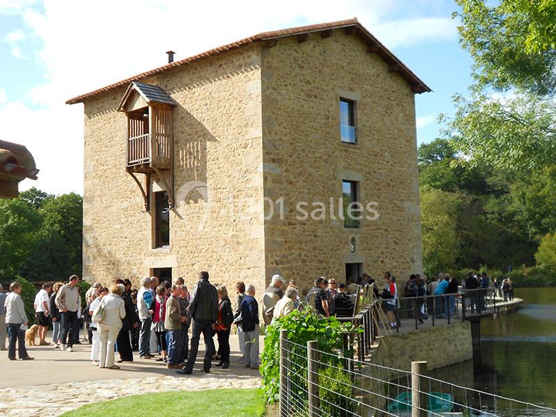 Groupe de personnes rassemblées devant un moulin en pierre près d'un plan d'eau, entouré de verdure.