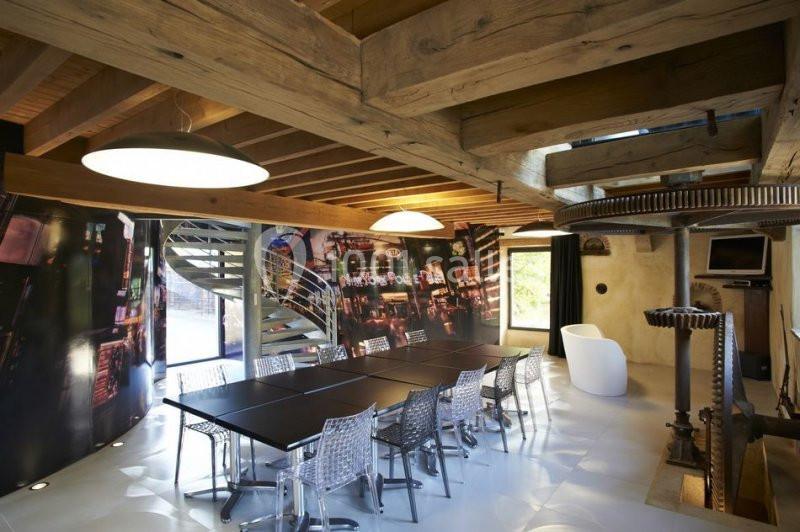 Salle de réunion avec table noire, chaises transparentes, poutres apparentes en bois et décoration industrielle.