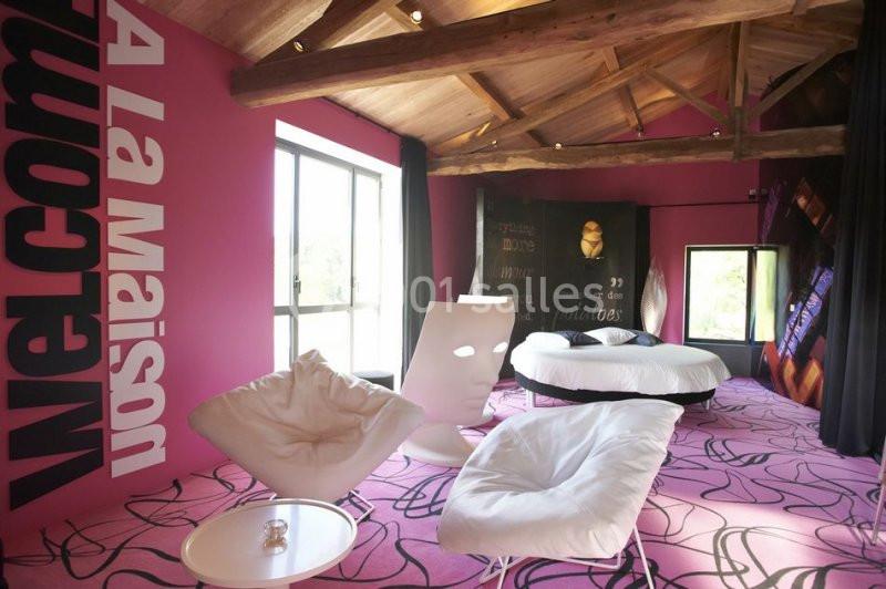 Chambre moderne avec murs roses, mobilier design blanc, lit rond et grandes fenêtres laissant entrer la lumière naturelle.