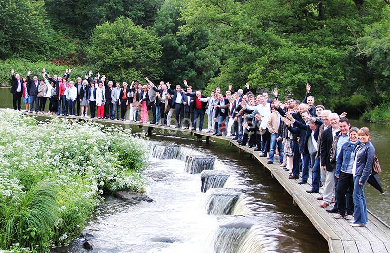 Un groupe de personnes pose sur une passerelle en bois au-dessus d'une rivière entourée de végétation.